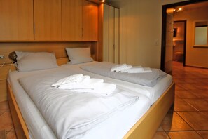 Quarto de hotel com duas camas, cada uma com toalhas brancas dobradas com capricho.