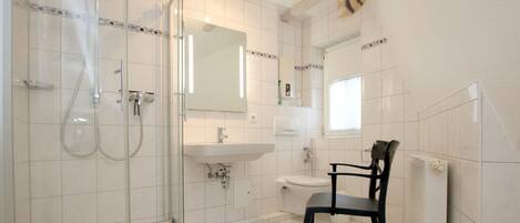 A bathroom with a glass-enclosed shower, a sink, a toilet, and a chair.