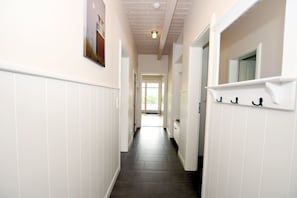 Een gang met witte plint, een lamp en een deur naar een lichte kamer.