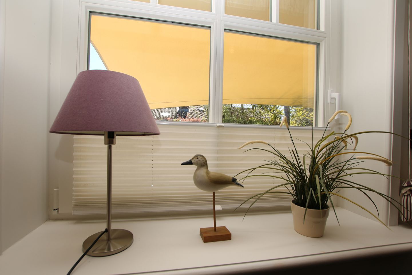 Une lampe, une plante en pot et une figurine de canard sur un rebord de fenêtre.