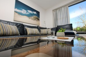 Una sala de estar moderna con un sofá de cuero negro, una mesa de centro de vidrio y un ventanal con cortinas.