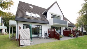 Een tweelaags huis met een overdekte veranda, een houten schutting en een gazon.