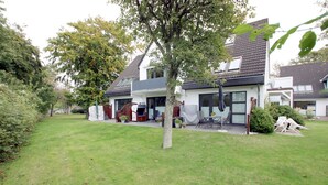 Een woonhuis met een verzorgd gazon, een terras met tuinmeubilair en een overdekt gebied met een barbecue.