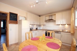 A modern kitchen with light-colored cabinets, a wooden dining table with pink placemats, and a chalkboard sign on the wall.