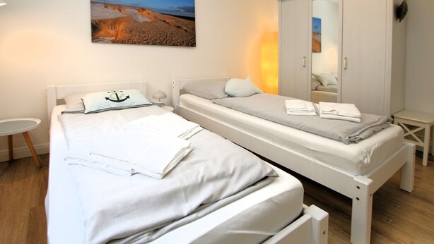 A twin room with two beds, a wardrobe, a small table, and a painting on the wall. - Strandstraße 8, Whg. 14, Green Eilun - terraced end house with approx. 75m² over 4 floors (Wyk auf Föhr)