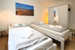 Quarto duplo com duas camas, um guarda-roupa, uma mesinha e um quadro na parede.