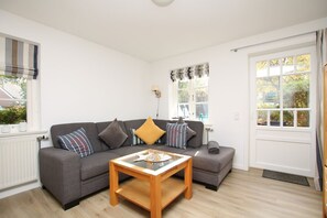 A modern living room with a grey sofa, a wooden coffee table, and a window with curtains. - Strandstraße 8, Apt. 14, Green Eilun - Corner townhouse with approximately 75 m² spread over 4 floors (Wyk auf Föhr)