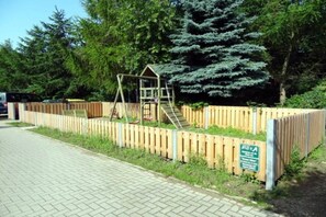 A playground with a wooden fence, a swing set, and a slide. - Strandstraße 8, Apt. 14, Green Eilun - Corner townhouse with approximately 75 m² spread over 4 floors (Wyk auf Föhr)