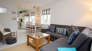 A living room with a sofa, a coffee table, a dining table with chairs, and a kitchen in the background. - Strandstraße 8, Whg. 14, Green Eilun - terraced end house with approx. 75m² over 4 floors (Wyk auf Föhr)