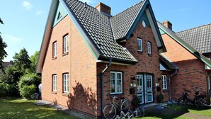 A two-story brick house with a steeply pitched roof, a front porch, and a bicycle parked outside. - Strandstraße 8, Whg. 14, Green Eilun - terraced end house with approx. 75m² over 4 floors (Wyk auf Föhr)