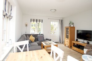 A living room with a sofa, a coffee table, a TV, and a cabinet. - Strandstraße 8, Apt. 14, Green Eilun - Corner townhouse with approximately 75 m² spread over 4 floors (Wyk auf Föhr)