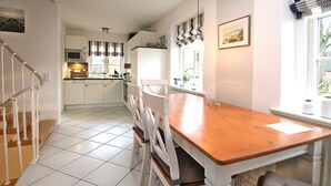 A kitchen with white cabinets, a wooden dining table, and a staircase with white railings. - Strandstraße 8, Whg. 14, Green Eilun - terraced end house with approx. 75m² over 4 floors (Wyk auf Föhr)