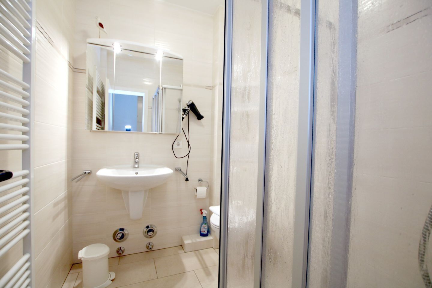 A bathroom with a sink, mirror, towel rack, shower, and toilet.
