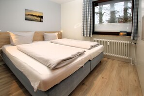 Ein Doppelbett mit Kopfteil, ein Fenster mit Vorhängen, ein Heizkörper und ein Wandbild.