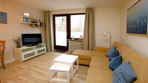 A living room with a sofa, a TV, a small table, and a bookshelf. - Badestraße 80, Whg. 1, Goting Hus - Newly renovated apartment on the mezzanine floor, (Wyk auf Föhr)