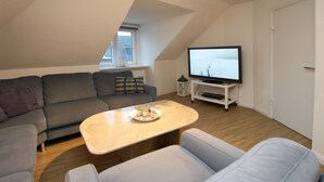 Ein modernes Wohnzimmer mit einem grauen Sofa, einem weißen Couchtisch und einem Fernsehgerät auf einem weißen Schrank.