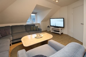 Een moderne woonkamer met een grijze bank, een witte salontafel en een televisie op een witte dressoir.