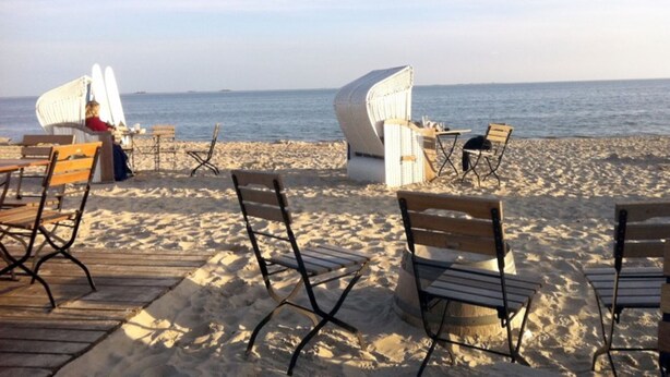 Un área de estar frente a la playa con sillas de madera y mimbre, una terraza de madera y vista al océano.