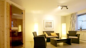 Una habitación con sofá, dos sillones, una mesa de centro, un cuadro en la pared y una ventana con cortinas.