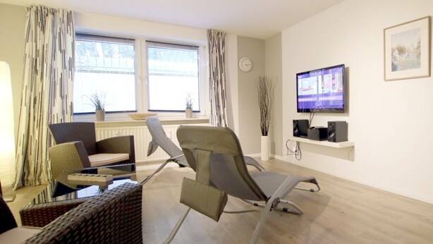 Una sala de estar moderna con un sofá, dos sillones, un televisor y una ventana con cortinas.