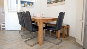 Un área de comedor con una mesa de madera, sillas negras y un banco. Se observan obras de arte en la pared y un refrigerador al fondo.