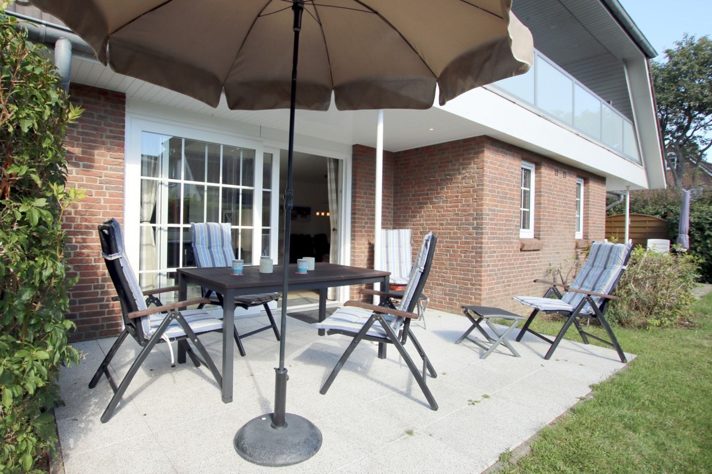 Eine Terrasse mit Tisch und Stühlen, einem Sonnenschirm und einem Backsteinhaus im Hintergrund.