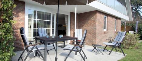 Eine Terrasse mit Tisch und Stühlen, einem Sonnenschirm und einem Backsteinhaus im Hintergrund.
