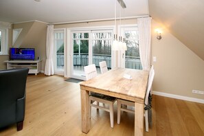 Ein Essbereich mit Holztisch und Stühlen, einem Fernseher und einem Balkon mit Geländer.