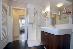 A modern bathroom with a glass shower enclosure, a vanity with a mirror, and a toilet visible in the adjacent room. - Starklef 34a, Whg. 2, Huus Starklef - Komfort Ferienwhg. in Wyk, 4 Personen, OG in 2- Familienhaus, (Wyk auf Föhr)