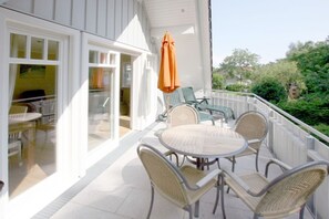 A balcony with wicker chairs and a table, a glass door leading inside, and an orange umbrella. - Starklef 34a, Whg. 2, Huus Starklef - Komfort Ferienwhg. in Wyk, 4 Personen, OG in 2- Familienhaus, (Wyk auf Föhr)