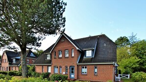 Une maison à deux étages, construite en briques, avec un toit à pignon, un porche à l’avant et un jardin bien entretenu.