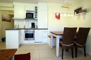Uma cozinha compacta com armários brancos, micro-ondas, fogão e um espaço de jantar com duas cadeiras e uma mesa.
