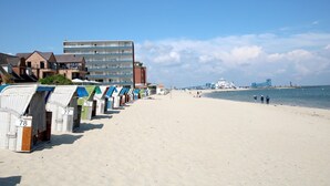 Una playa con cabañas de playa numeradas del 75 al 78, un edificio grande y un terminal de ferry al fondo.