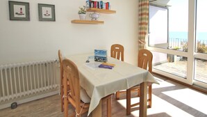 A dining area with a table, chairs, a radiator, a window with a view, and a shelf with books and a teapot. - Sandwall 11a, Whg. 2 "Gästehaus Gorch Fock" - vacation apartment with 2 rooms on (Wyk auf Föhr)