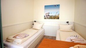 A small, single-room accommodation with two beds, a wooden table, and a beach-themed wall art. - Sandwall 11a, Whg. 2 "Gästehaus Gorch Fock" - vacation apartment with 2 rooms on (Wyk auf Föhr)