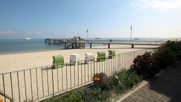 A beach with a pier, a sandy shore, and a fenced area with green and white structures. - Sandwall 11a, Whg. 2 "Gästehaus Gorch Fock" - vacation apartment with 2 rooms on (Wyk auf Föhr)