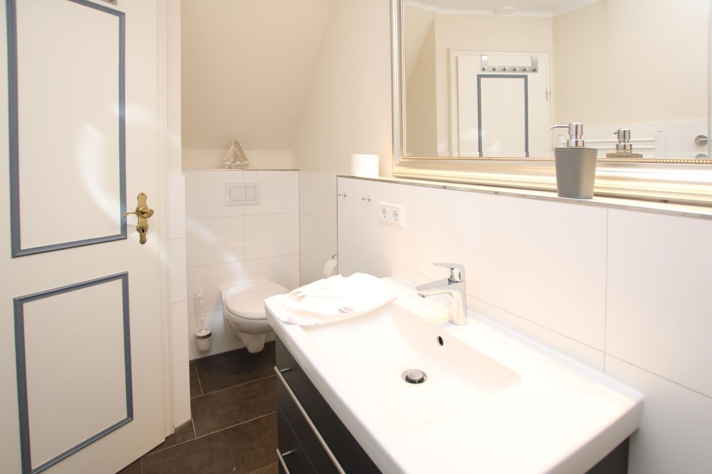 A bathroom with a white sink, a mirror, a toilet, and a door with a brass handle.