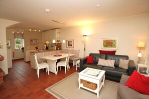 Ein Wohnzimmer mit Sofa, einem Esstisch mit Stühlen, einer Küchenzeile und einer Lampe.