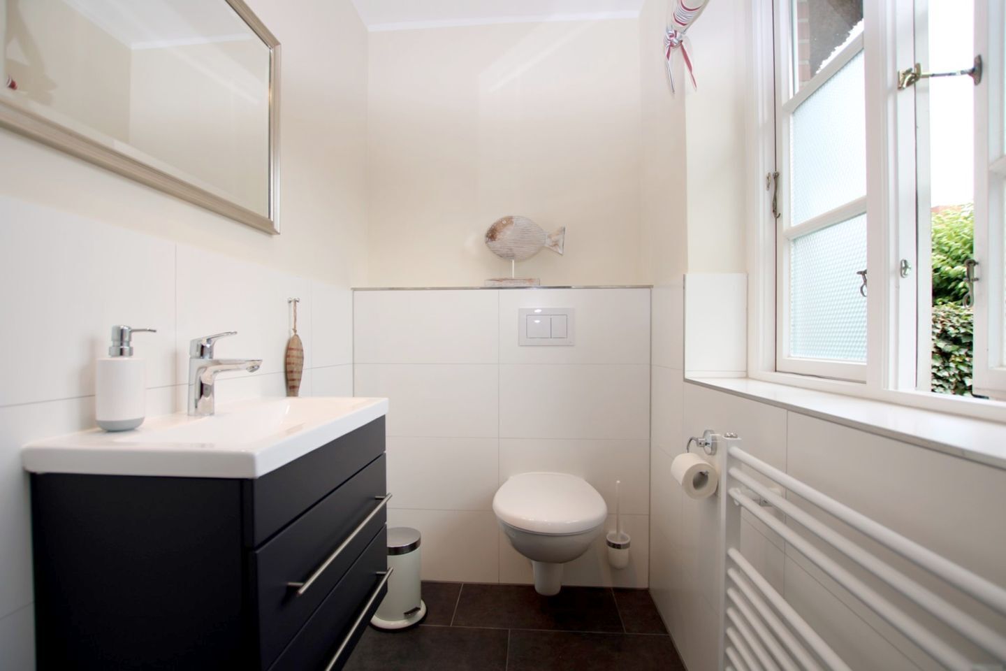 Une petite salle de bain comprenant des toilettes, un lavabo avec un distributeur de savon, un miroir et une fenêtre.