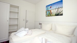 A bedroom with a bed, a white wardrobe, a door, and a painting of a beach scene. - Sandwall 11a, Whg. 3 "gästehaus Gorch Fock" - Ferienwohnung mit 2- Zimmern auf ca. 42m² mit Direktem (Wyk auf Föhr)