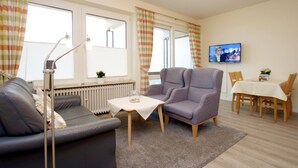 A living room with a sofa, armchair, table, and dining area with chairs and a TV. - Sandwall 11a, Whg. 3 "gästehaus Gorch Fock" - Ferienwohnung mit 2- Zimmern auf ca. 42m² mit Direktem (Wyk auf Föhr)