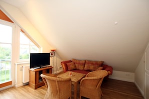 Een knus loft slaapkamer met een groot raam, een flatscreen televisie, een rode bank en rieten stoelen.