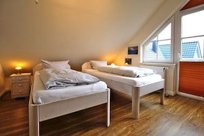 Een slaapkamer met twee eenpersoonsbedden, een nachtkastje, een raam met zonwering en een radiator.