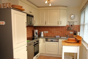 A compact kitchen with white cabinets, a stainless steel refrigerator, a coffee maker, and a sink.