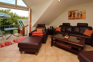Ein geräumiger Wohnbereich mit einer Couch, Hocker und Couchtisch, ein Balkon mit Tisch und Stühlen sowie ein Bild an der Wand.