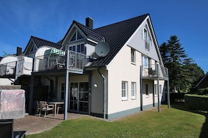 Kaksikerroksinen talo, jossa on parveke, satelliittiantenni ja ulkotila, jossa on ulkokalusteita.