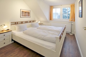 A bedroom with a bed, bedside tables, a nightstand, a window with curtains, and a radiator.