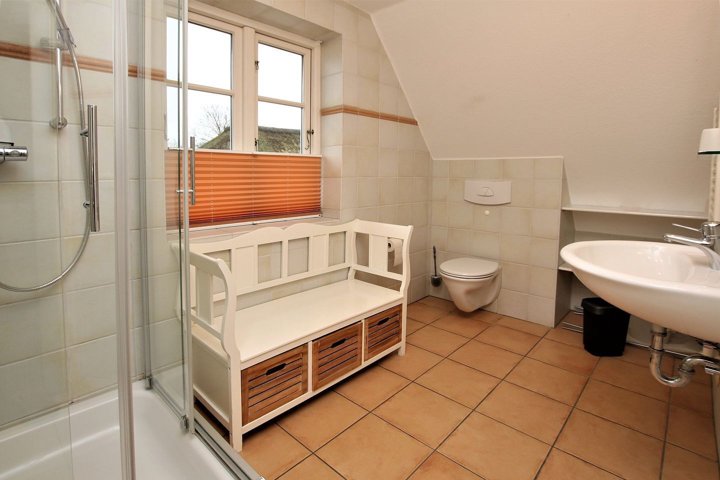A bathroom with a shower, toilet, sink, and a bench with storage drawers.