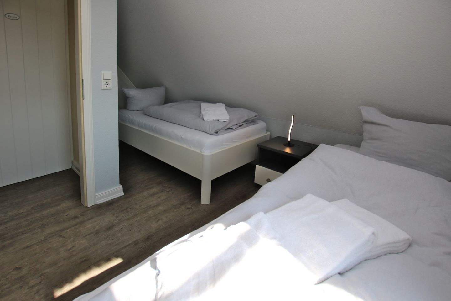 A bedroom with a bed, a bedside table, a nightstand, and a door.