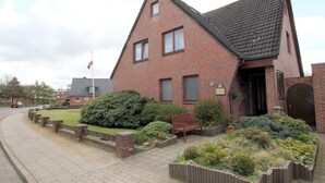Een gebouw van rode bakstenen met een steil dak, een wimpel en een bank in de tuin.